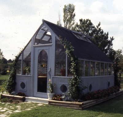 Redwood greenhouse stained gray with wood base and shade cloth